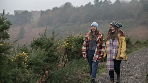 Visitors taking the Hunter's Path along the top of the Teign Gorge down towards Fingle Bridge with Castle Drogo in the background.